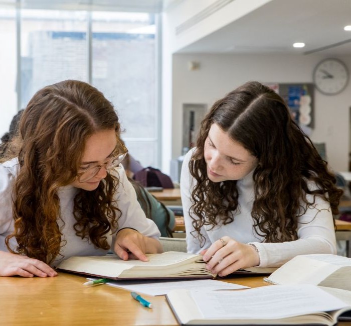 Two smiling female students taking a selfie while reading torah