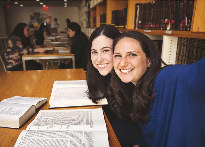 Two smiling female students taking a selfie while reading torah