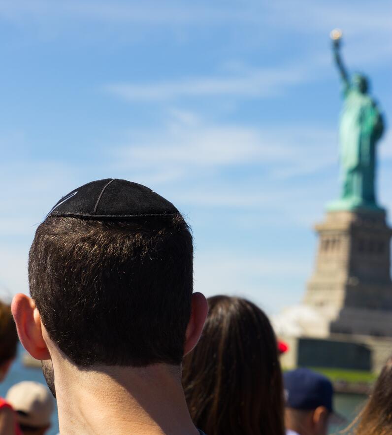 Male student with kippa in front of Statue of Liberty