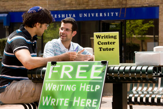 two men sitting at a table with a sign for free writing help