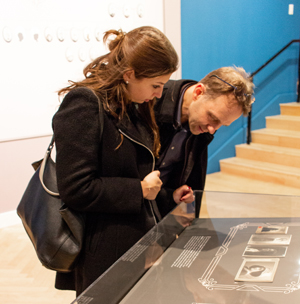 Lost & Found: A Family Album. Two people looking at photos in a display case.