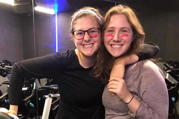 Two women pose in the gym for Sweat 4 Tzedakah