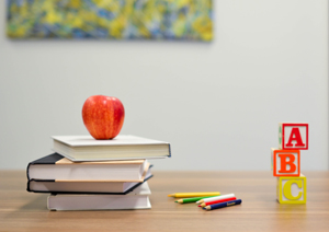 Apple on a pile of books with A-B-C blocks on the desk next to it